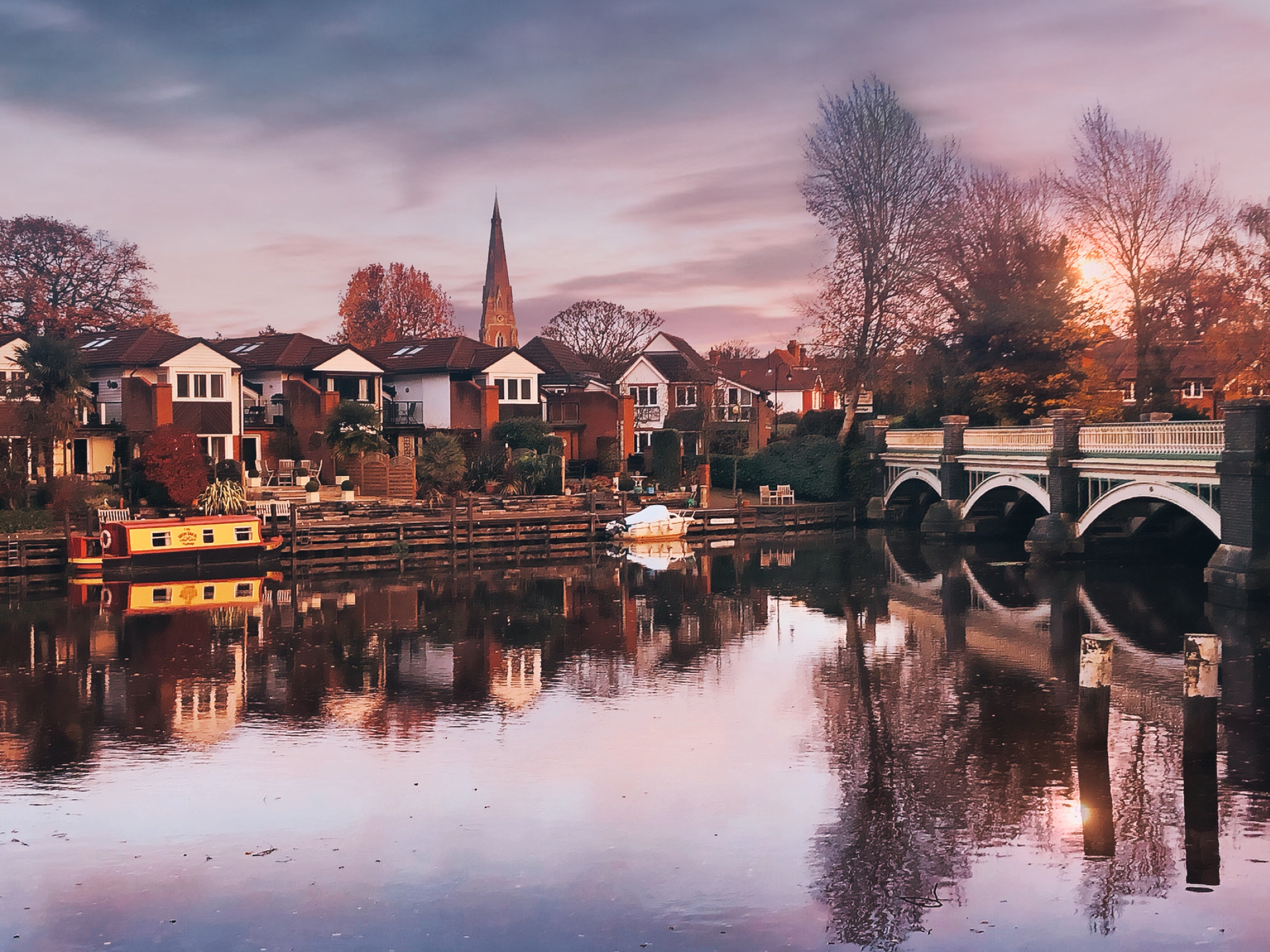 Old bridge over the River Wey at Weybridge at dusk, with riverside houses reflected in still water.